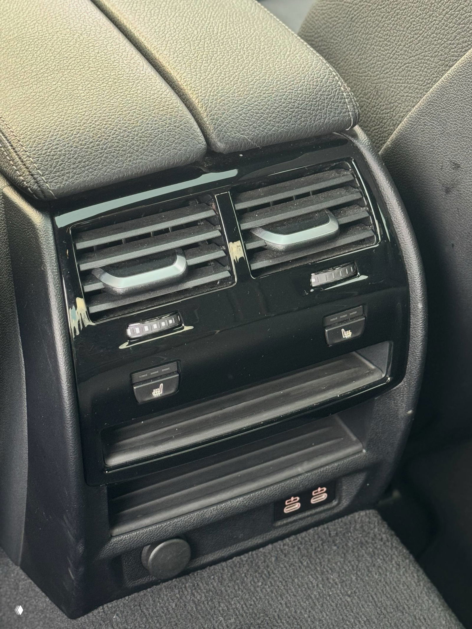 Крупный план задней консоли BMW 520i: воздуховоды, кнопки подогрева сидений и USB‑разъёмы, аккуратная отделка и следы использования на коврике.