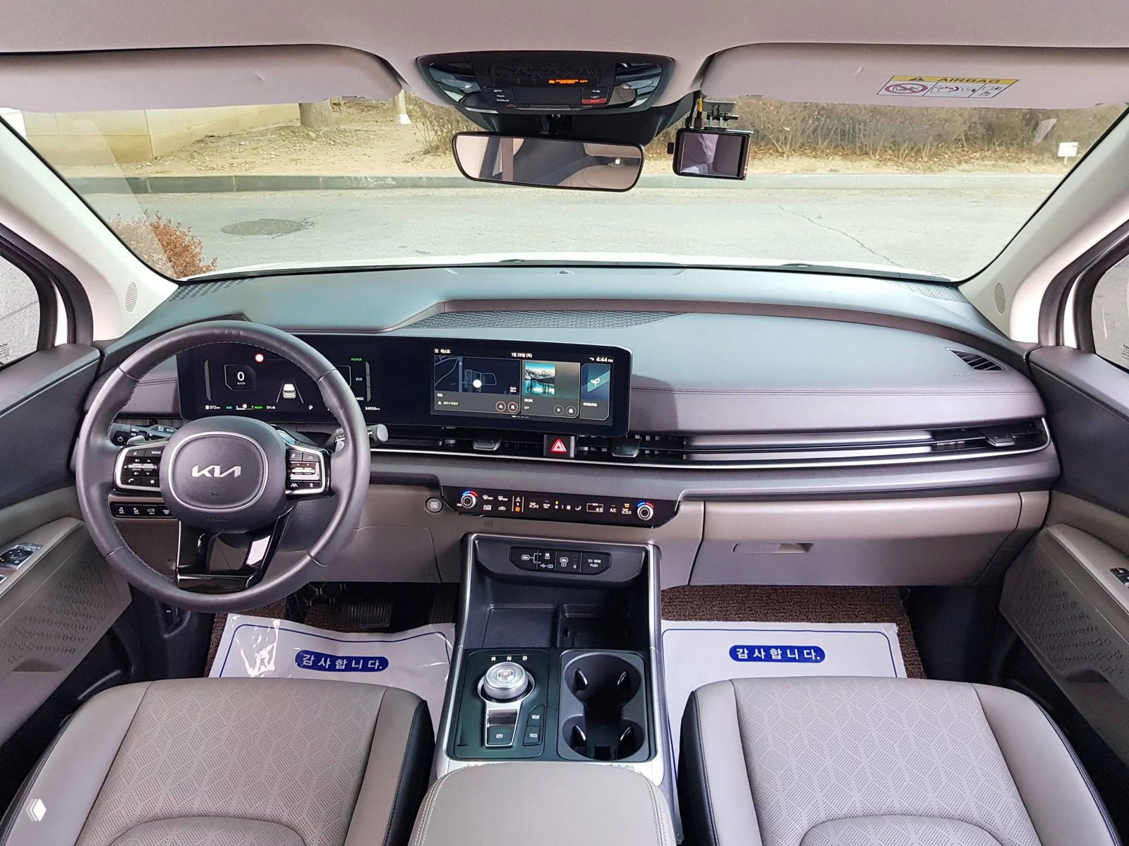 Панорамный вид торпедо и передней панели KIA Carnival: большой экран мультимедиа и салон премиального вида в нейтральных тонах.