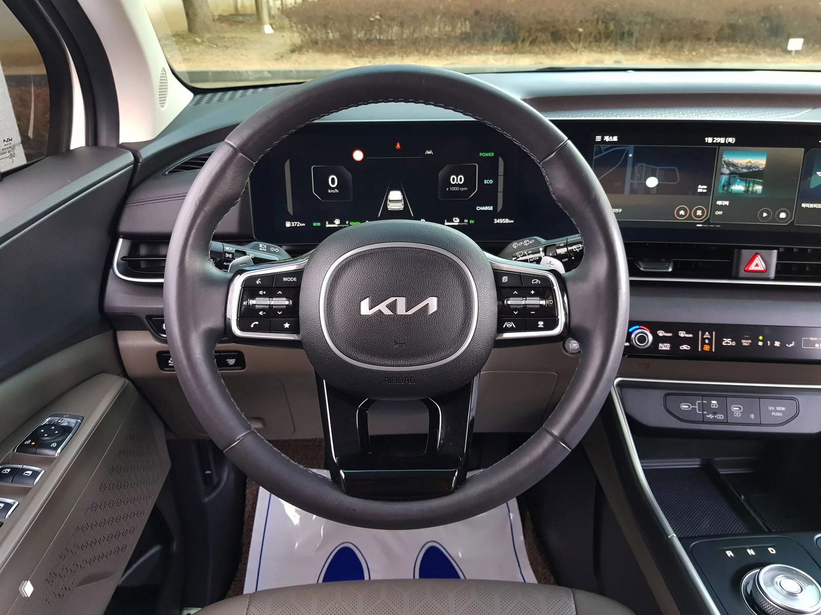 Крупный план приборной панели и рулевого колеса KIA с логотипом, на дисплее цифровая приборная панель и индикаторы гибридной системы.