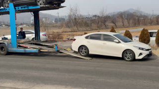 Белый автомобиль на рампе автовоза во время погрузки, крупный план процесса посадки машины на платформу перед отправкой.