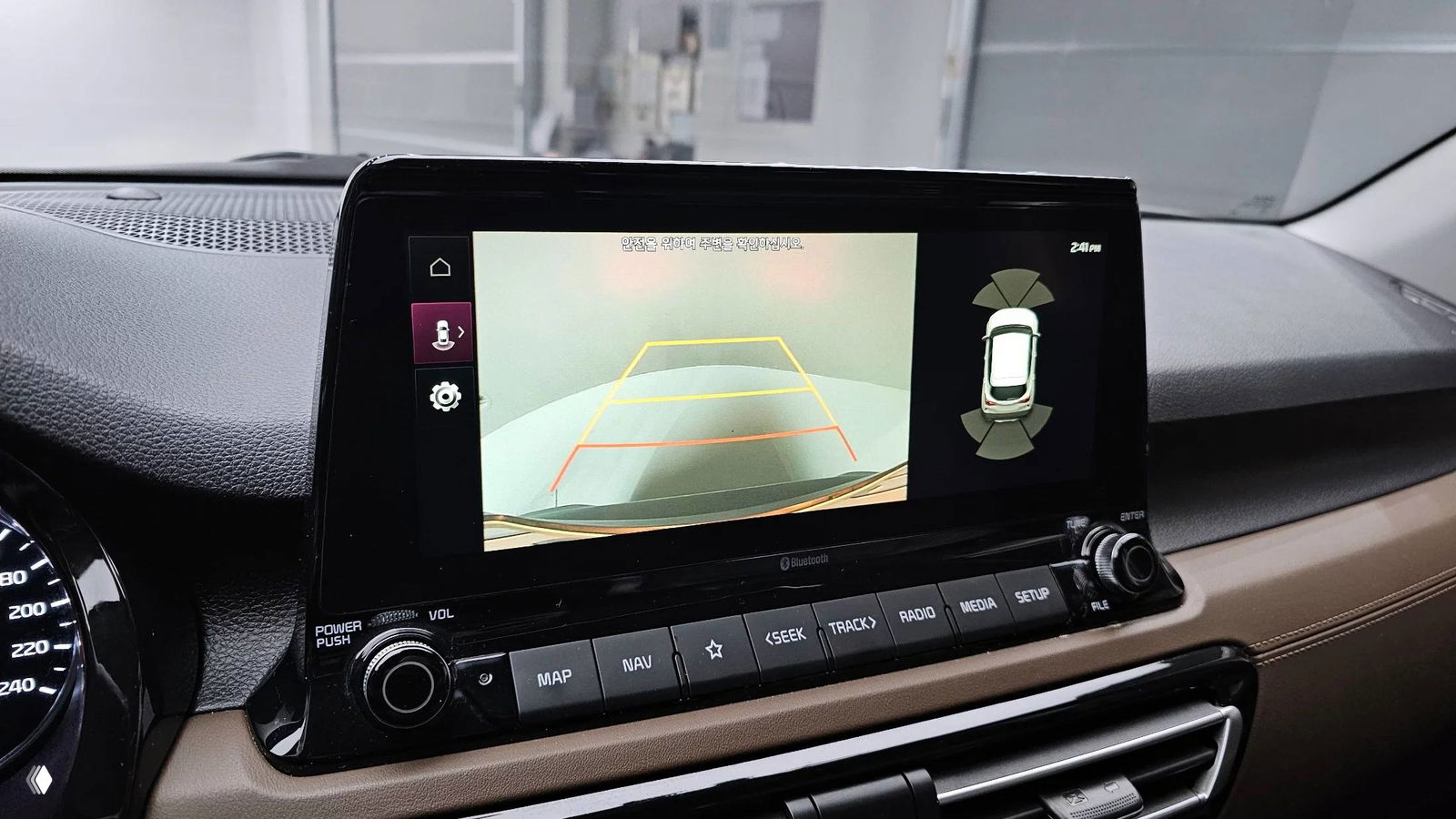 Экран мультимедиа KIA Seltos показывает изображение со камеры заднего вида с траекториями парковки и схемой окружения автомобиля.