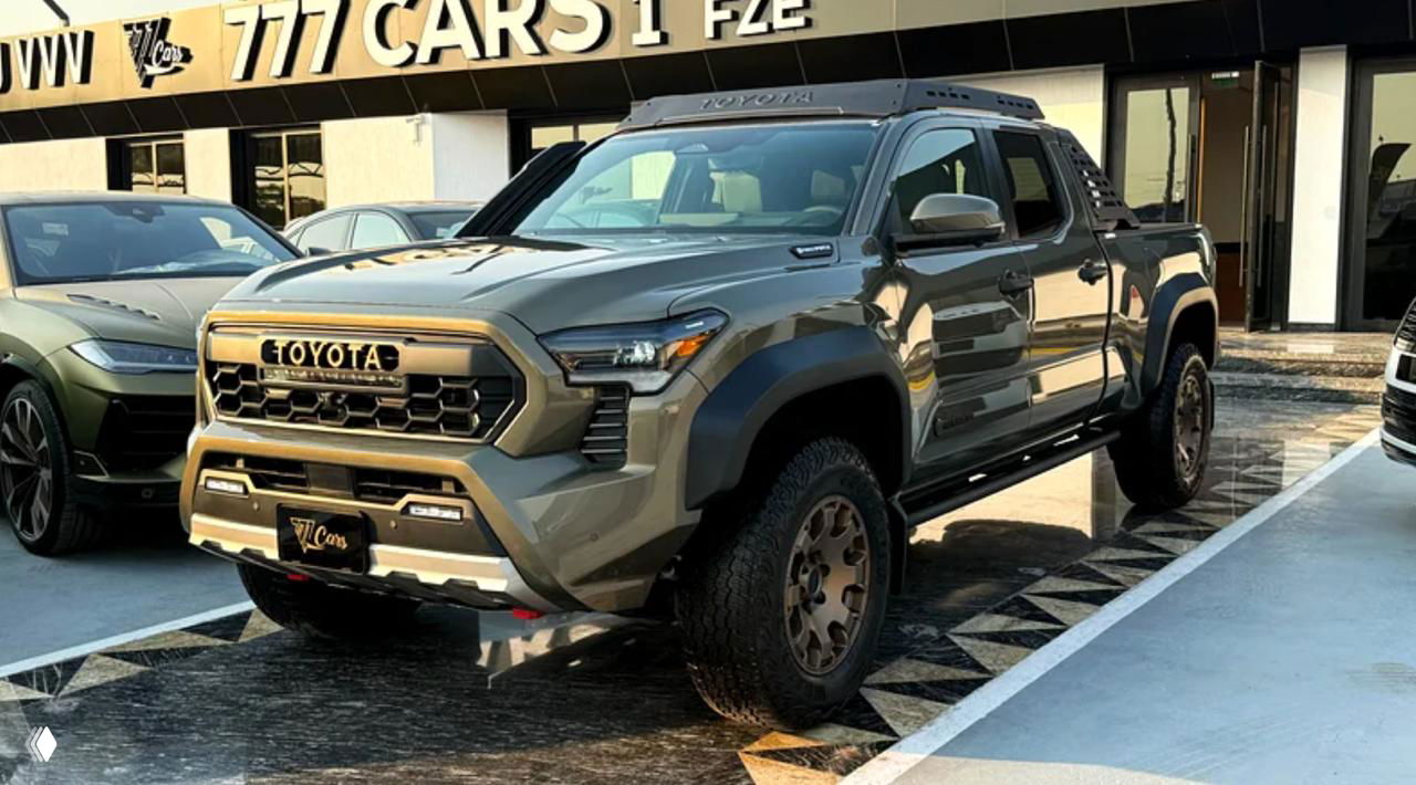 Серебристая Toyota Tacoma TRD 2025 на выставочной площадке дилера, боковой ракурс с видимыми внедорожными колесами и усиленными крыльями.