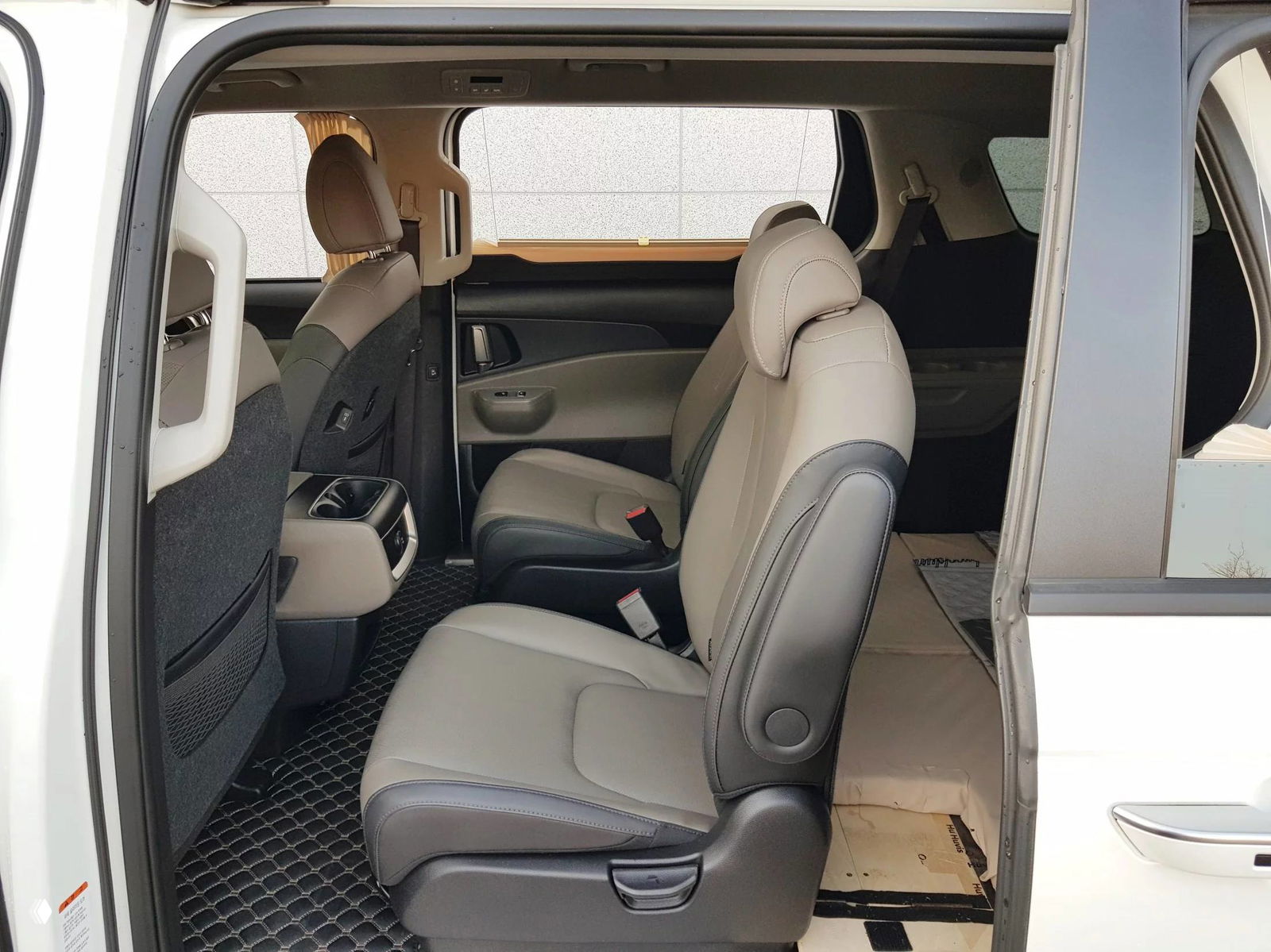 Средний ряд сидений KIA Carnival: отдельные кресла, пространство для ног и коврики, вид на открывающуюся раздвижную дверь из салона.