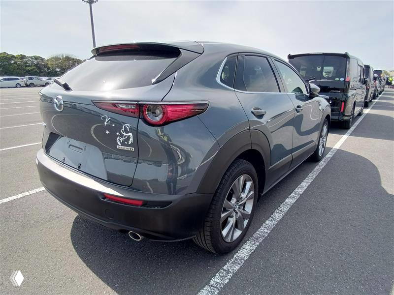 Фото Mazda CX-30 2023 — задний вид автомобиля на стоянке, видна кормовая часть и соседние машины на ярде, состояние кузова хорошее.