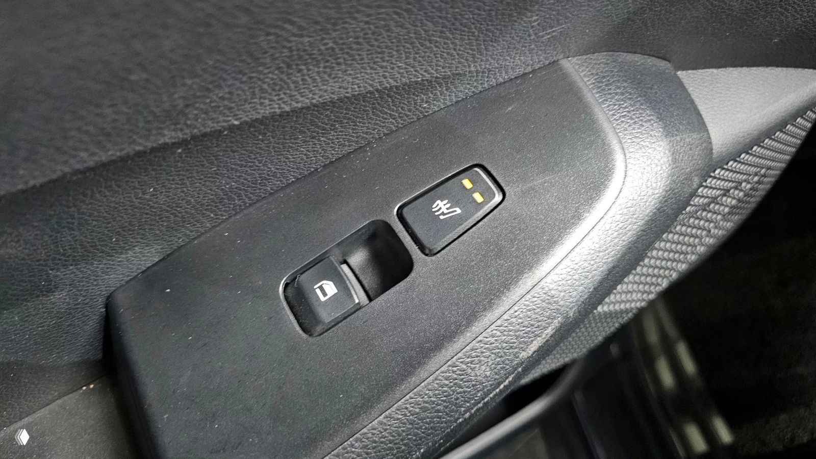 Крупный план панели управления на двери: кнопка блокировки и регулировки зеркал с подсветкой, видна текстура пластика и износ у рукояти.