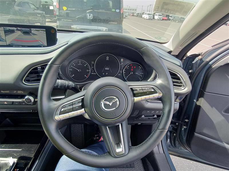Крупный план рулевого колеса и приборной панели Mazda CX-30 2023 — спидометр, тахометр и элементы управления в салоне автомобиля.