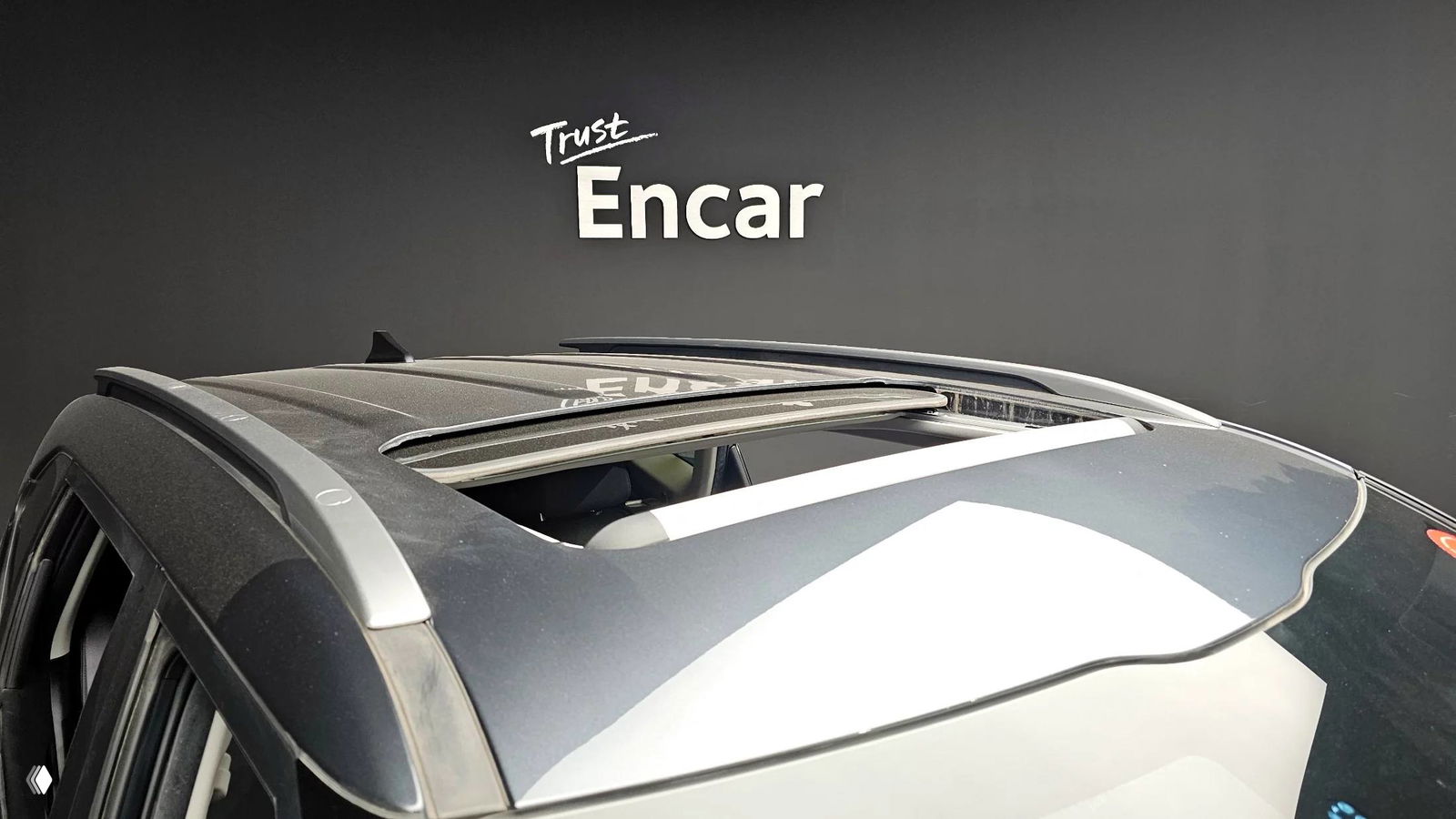 Вид на люк и рейлинги на крыше KIA Seltos: частично открытый сдвижной люк и алюминиевые рейлинги на фоне стен студии.