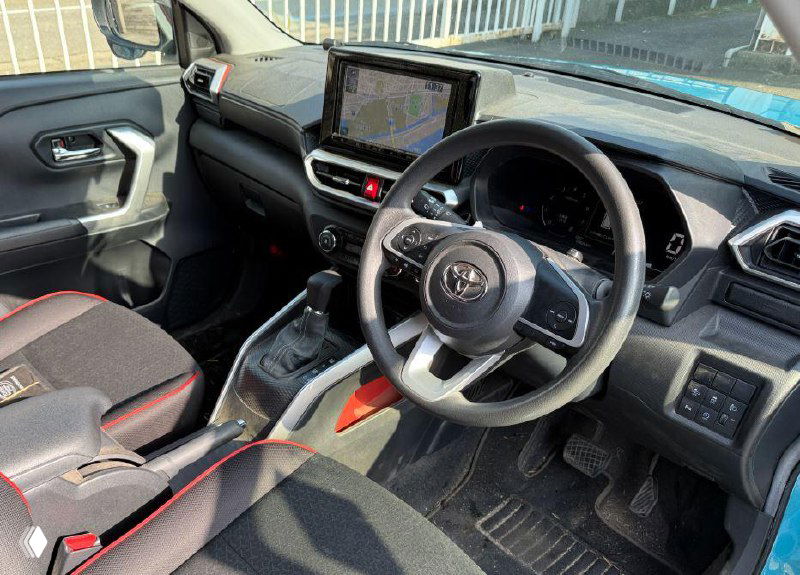 Искажённое фото салона с видом рулевого колеса и центральной консоли Toyota Raize; изображение содержит цифровые артефакты и шумы.