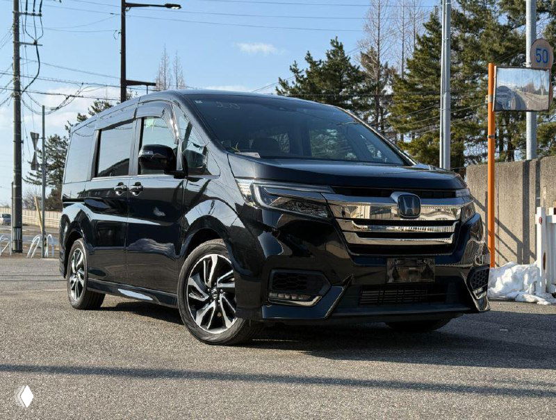 Чёрная Honda Stepwgn RP3 2018 на открытой парковке в Японии, фронтально-боковой ракурс, отражения на лаке и вид колёс.