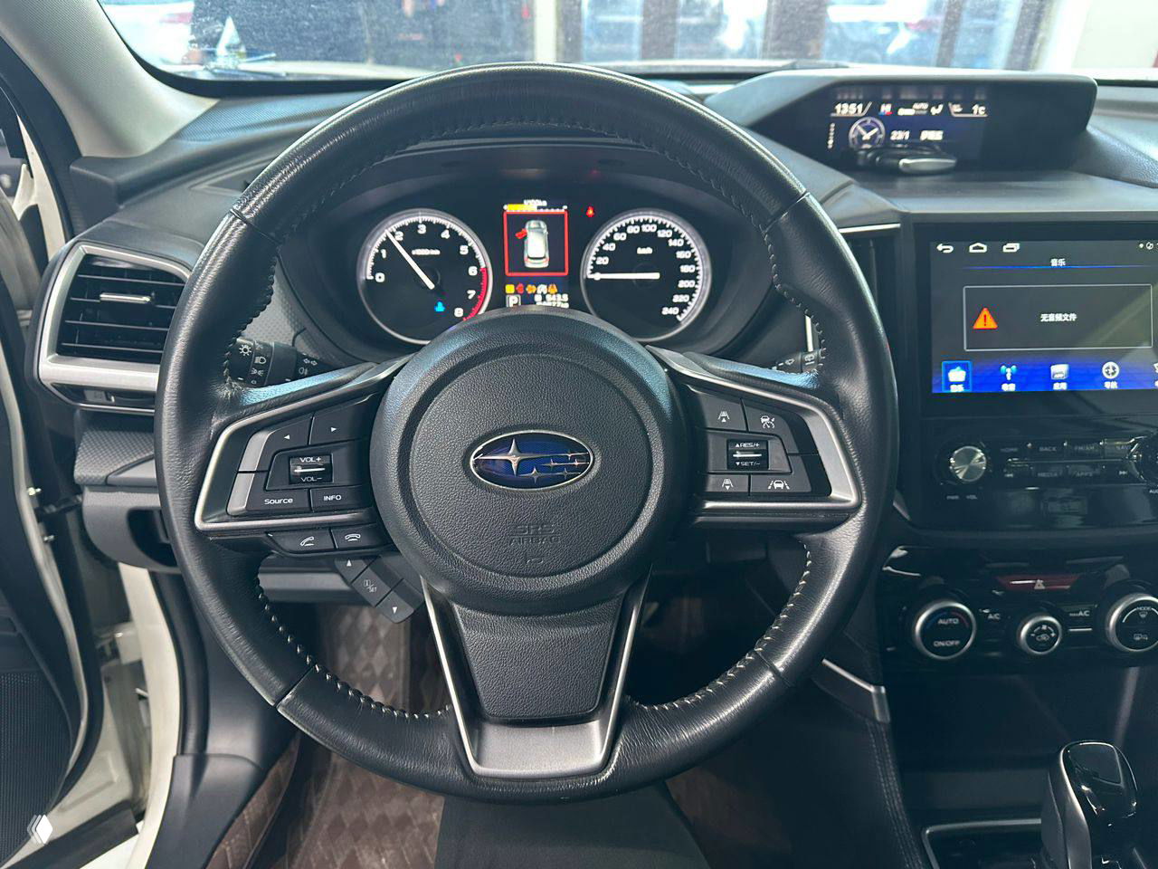 Крупный план рулевого колеса Subaru с логотипом, щиток приборов и экран мультимедиа, чёткое фото элементов управления и приборной панели.