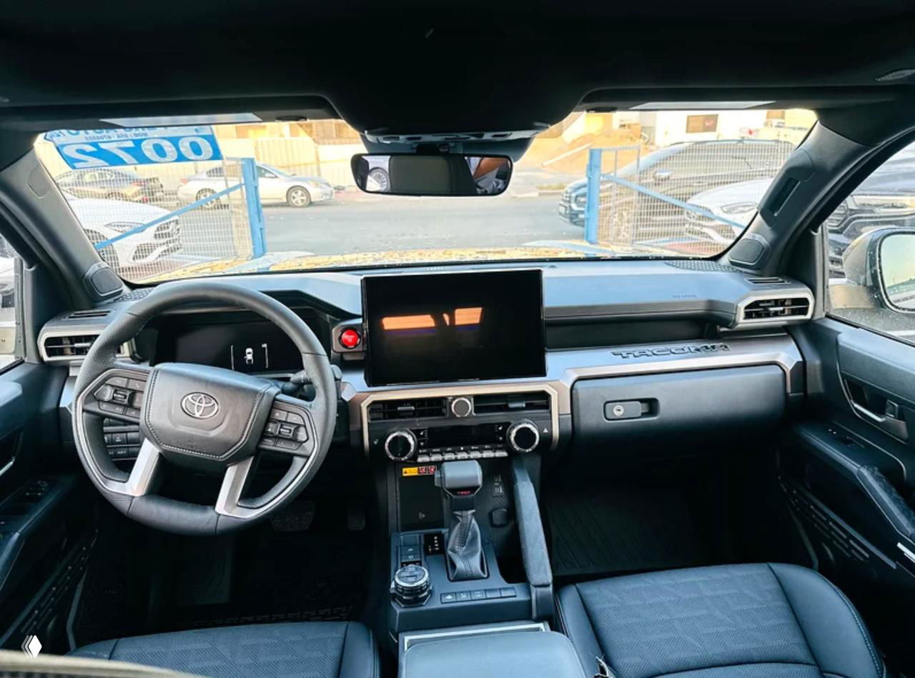 Интерьер Toyota Tacoma: панель приборов и мультимедийный экран в центре торпедо, руль с логотипом Toyota и селектор АКПП на переднем плане.