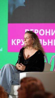 Вероника Крутильникова на сцене конференции PSYCHOLOGIES с микрофоном, обсуждает тревогу и подготовку к дню — зелёный фон