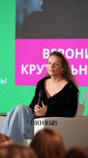Вероника Крутильникова сидит на сцене с микрофоном на фоне баннера конференции PSYCHOLOGIES, обсуждает идеи отдыха и сохранения ресурсов.