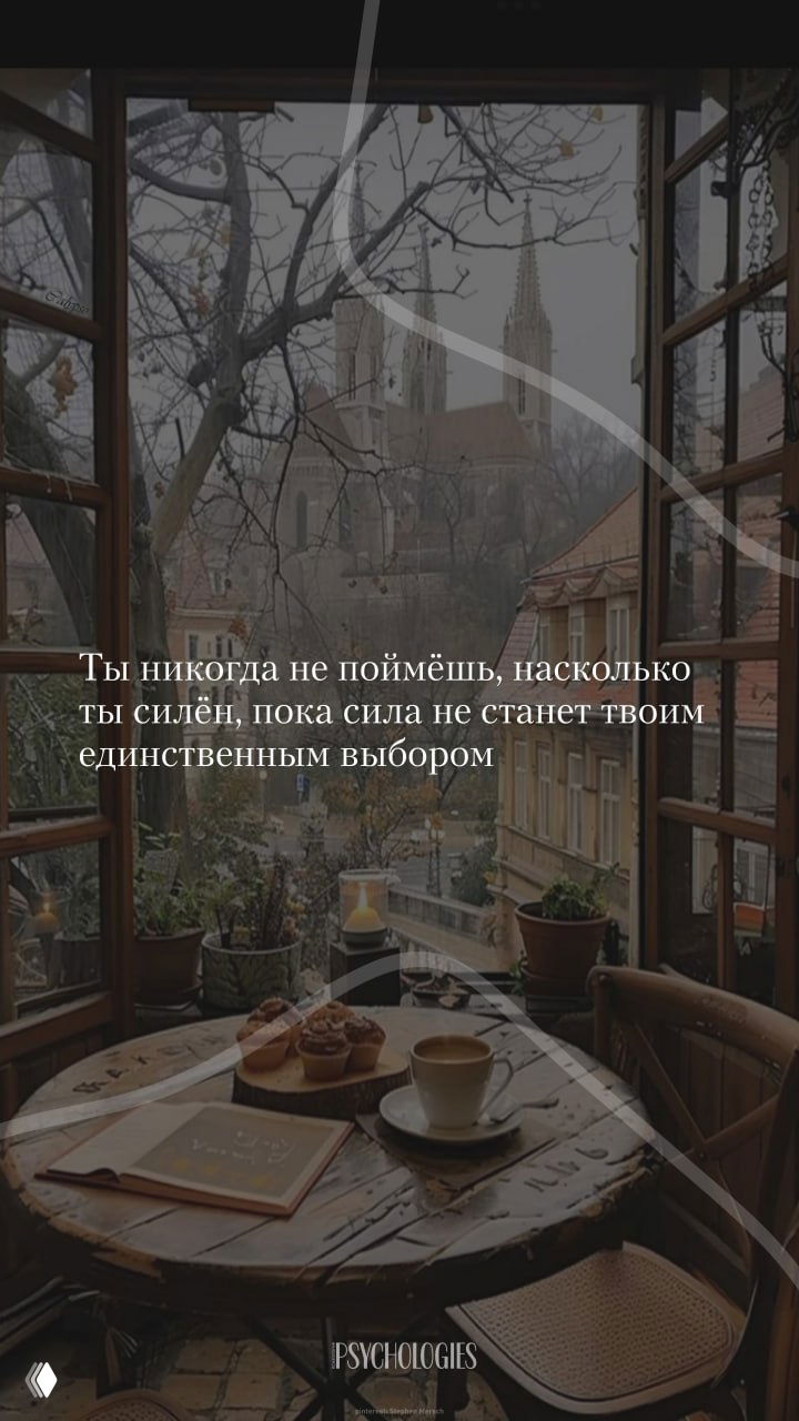 Фотография уютного уголка у окна: стол с чашкой кофе, кексами, блокнотом и растениями на фоне старинных домов и силуэта собора.