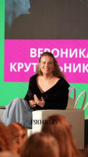 Вероника Крутильникова на сцене конференции PSYCHOLOGIES: полукрупный план, улыбается; впереди слушатели и яркая графика