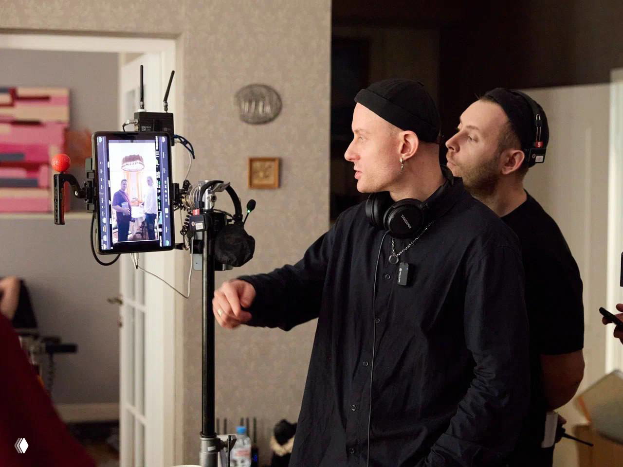 Рабочая сцена на площадке: режиссёр и звукорежиссёр смотрят на монитор на штативе; видно оборудование и кадрирование внутри квартиры‑сцены.