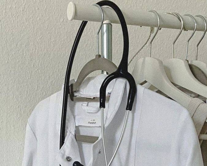 Стетоскоп и белый халат на вешалке в лёгком интерьерном фоне — медицинская атрибутика, символ врачебной профессии и научной практики.