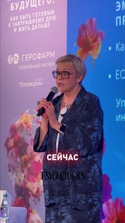 Женщина-лектор с микрофоном на сцене перед экраном с логотипом Psychologies и декоративными цветами, кадр во время трансляции.