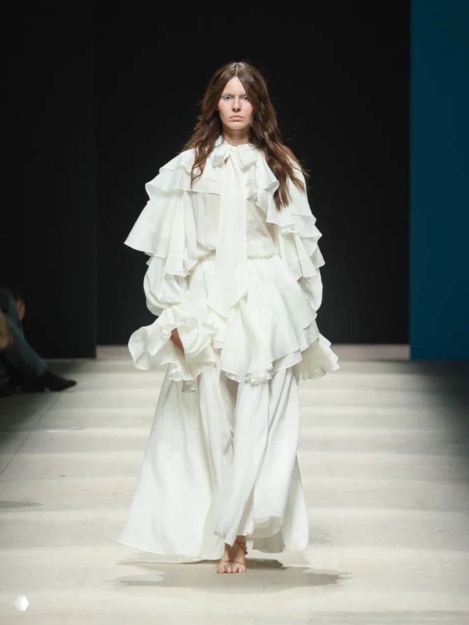 Модель в многослойном белом платье с рюшами и длинными рукавами, ретро‑футуристический образ Tatiana Kotova на подиуме.