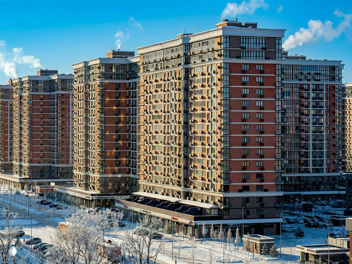 Панорамный фасад нескольких жилых корпусов микрорайона «Самолет» в солнечный зимний день, общий план застройки и автопарковка у дома.