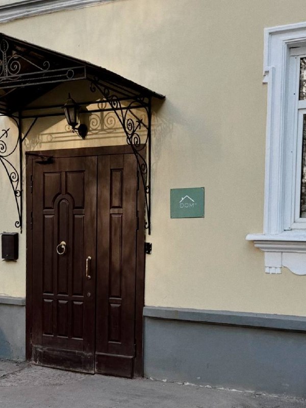 Фасад здания и входная дверь с декоративным наличником; снимок содержит цифровые артефакты и искажения на изображении, видно крыльцо.