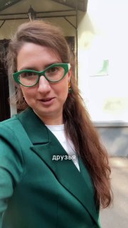 Селфи около шоурума: женщина в зелёных дизайнерских очках на фоне светло‑жёлтого двухэтажного здания с вывеской DOM у входа в шоурум.