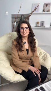 Женщина в светлом шоуруме сидит в кресле и демонстрирует очки O.D.L. Happy — крупный план оправы на фоне полок и декора.