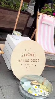 Стенд на маркете: круглая деревянная табличка, тазик с декоративными ромашками и розово‑белое пляжное кресло в зоне экспозиции.