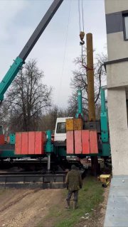 Стройплощадка: подъёмный кран и тяжёлая техника у фундамента нового дома, рабочие рядом, серая погода и стройматериалы