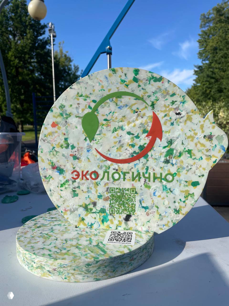 Круглые плиты и таблички из смешанного переработанного пластика с логотипом «Экологично», выставленные на столе демонстрации.