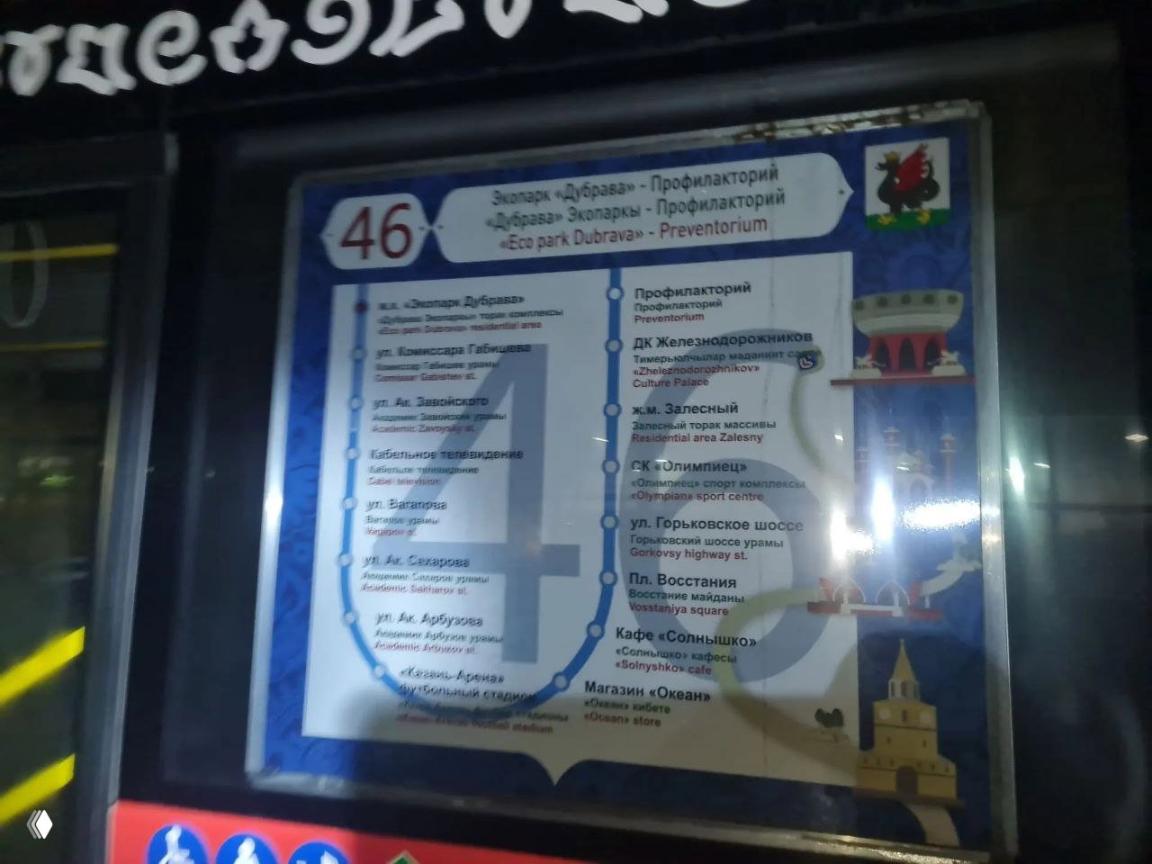 Окно другого автобуса с маршрутной схемой 46, отражения и элементы салона на фоне; плакат маршрута крупно виден через стекло.