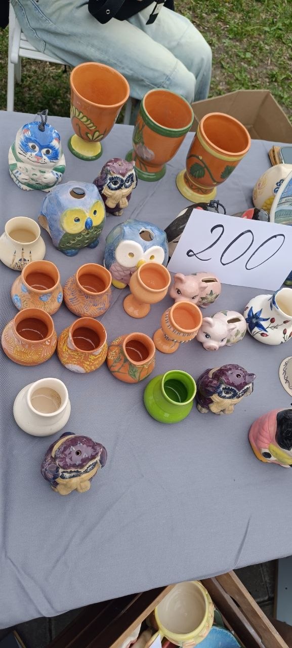 Стол с керамическими фигурками и расписными чашками, знак с ценой 200 рублей — ассортимент хендмейд и винтажа на ярмарке в парке.