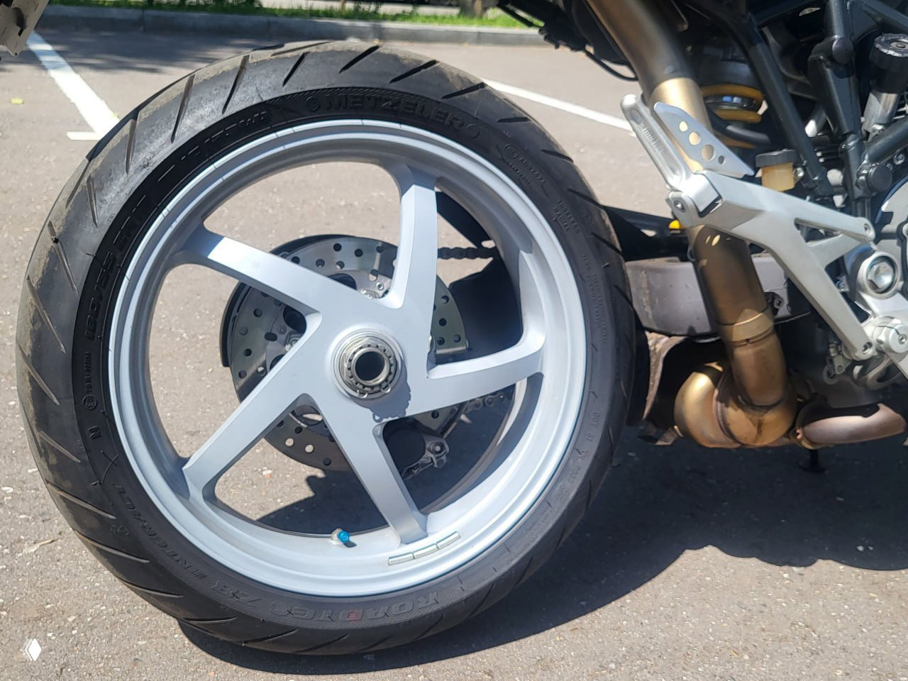 Крупный план заднего колеса и обода Ducati Multistrada 1000DS: видна резина, обод и часть выхлопной системы на стоянке. Фото для объявления и оценки состояния.