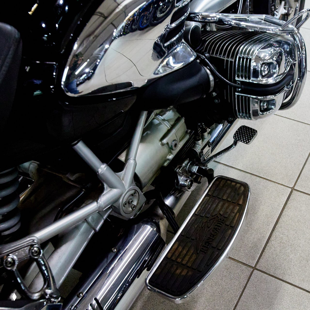Детали шасси и двигателя BMW R 1200 C: хромированные элементы, картер двигателя, подножка и ходовая часть на кафельном полу шоурума.
