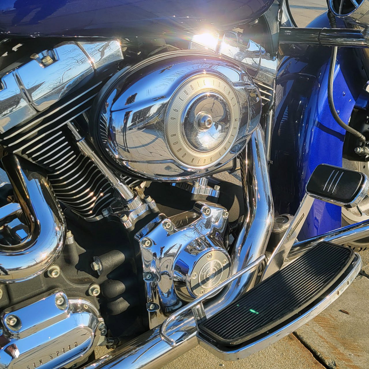 Крупный план шестерён и хромированных деталей двигателя TwinCam на синем кузове мотоцикла — отражения и блеск хрома на солнце.