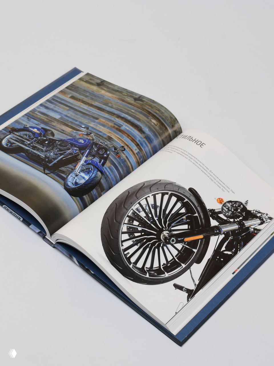 Разворот глянцевой книги: крупный план переднего колеса мотоцикла на фотографии и другой мотоматериал на соседней странице.