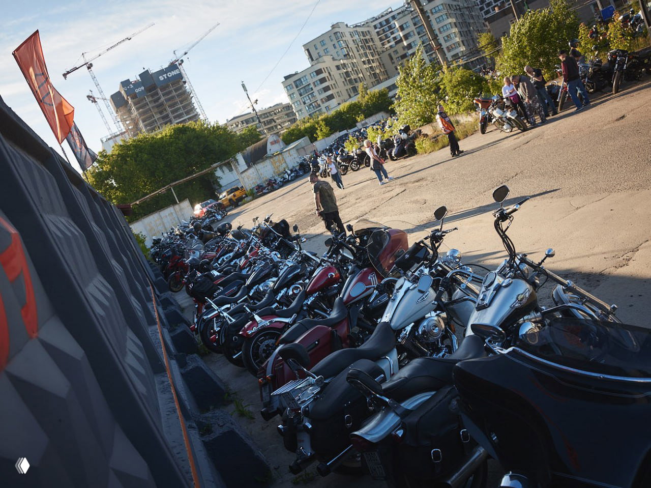 Промзона и большая парковка с рядом стоящими мотоциклами, в основном Harley-Davidson, выстроенные в один ряд у бетонного забора заведения.