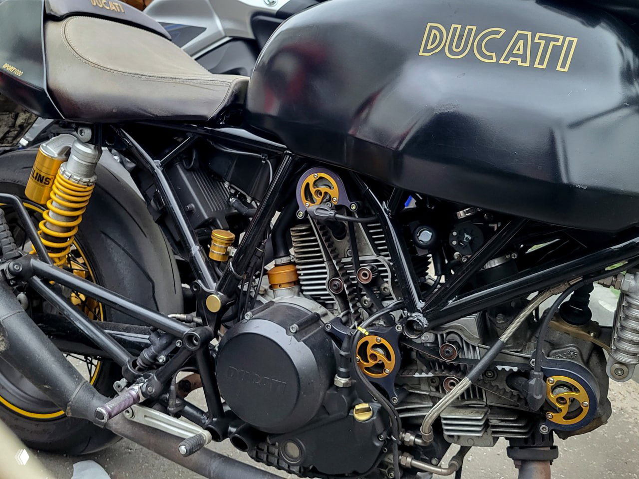 Фрагмент двигателя и рамы рядом с баком с надписью DUCATI — механика и индивидуальные элементы на трёхцилиндровом/двухцилиндровом мотоцикле на встрече клуба.