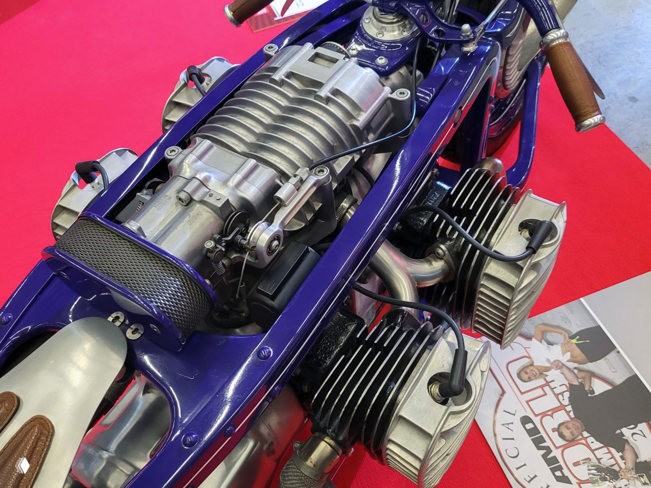 Синий кастом с открытым оппозитным или боксерным блоком цилиндров и фиолетово‑синей рамой, крупный план моторной группы на выставке.