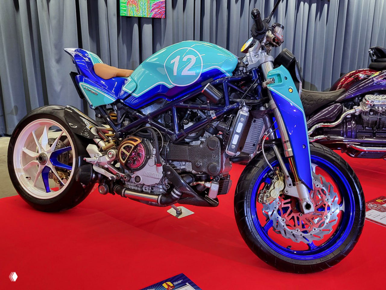 Хромированный дорожный чоппер с удлинённой вилкой и баком с надписью Harley Davidson, часть экспозиции на красном ковре в зале.