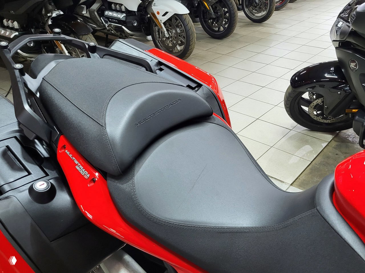Угловая фотография передней части мотоцикла Ducati Multistrada 1200 S: фара, ветровое стекло и панель приборов, салон магазина на заднем плане.