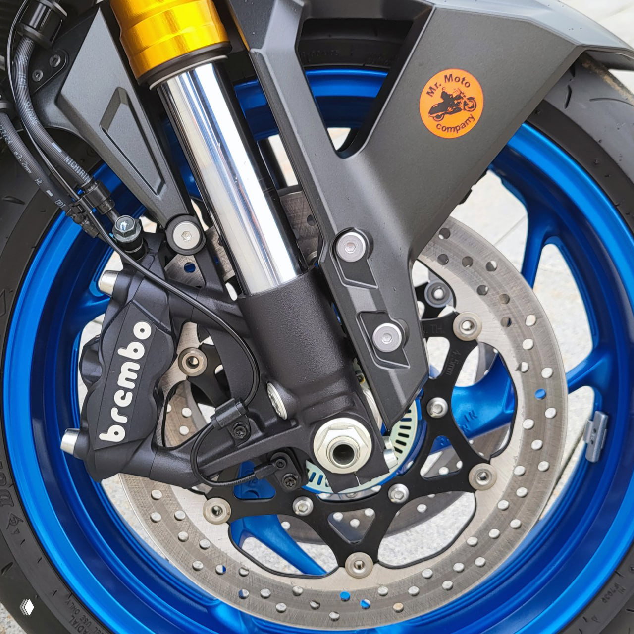 Крупный план переднего колеса и тормозной системы Suzuki GSXS1000GX: суппорт с маркировкой brembo и перфорированный тормозной диск.