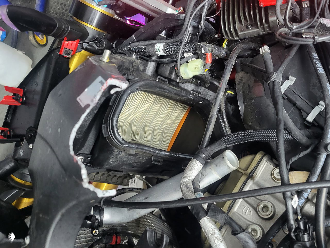 Крупный план повреждённого корпуса и воздушного фильтра Ducati Streetfighter V4 с порванными пластиковыми панелями и оголённой проводкой вблизи.