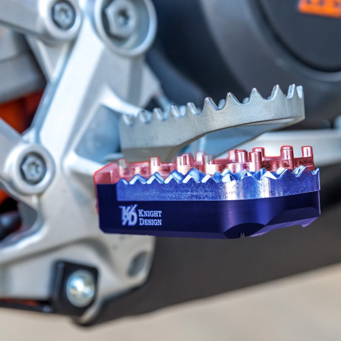 Крупный план мотокроссовой подножки с зубчатой поверхностью и сменной платформой; видна фиолетово‑синяя база и болты.