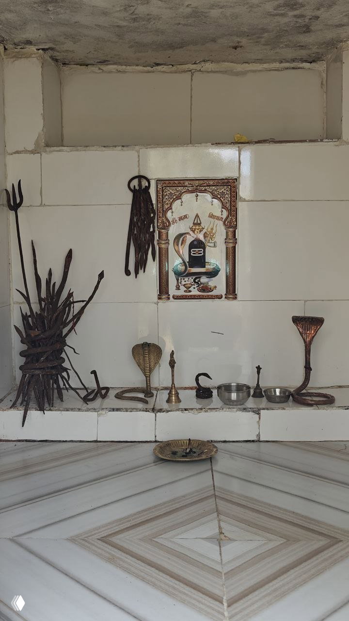 Небольшой домашний алтарь с изображением и индуистскими ритуальными предметами на плиточной стене — религиозная атмосфера места.