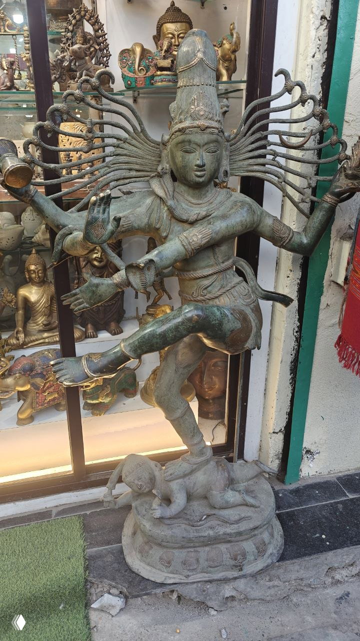 Бронзовая статуэтка Натарджи (танцующего Шивы) в лавке сувениров — индуистская символика и местное ремесло рядом с храмовой утварью.