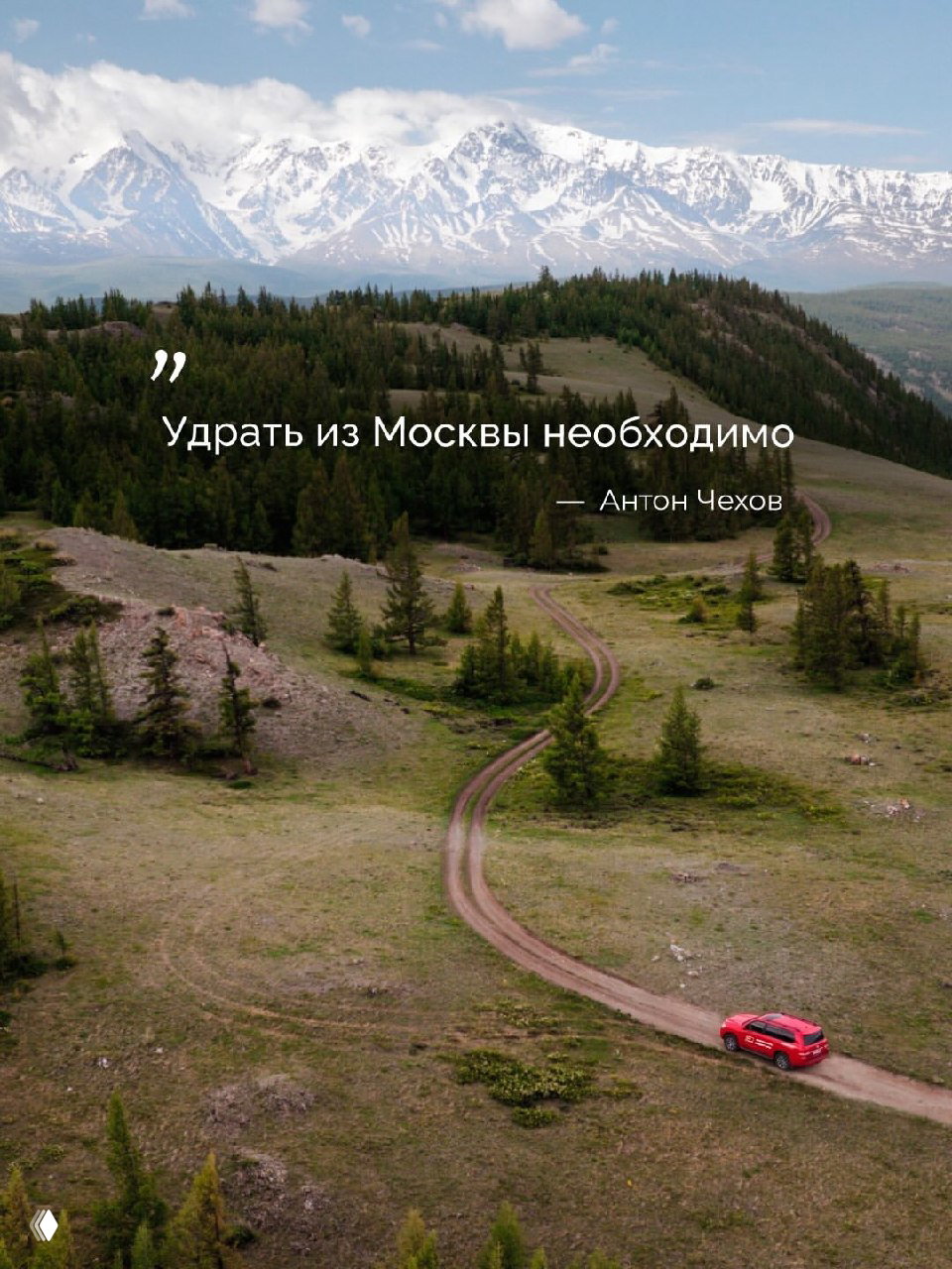 Аэрофотоснимок горной местности и извилистой грунтовой дороги, по которой едет красный внедорожник; на фоне видны горы и небо.