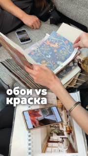 Руки дизайнера листают каталоги обоев и образцы тканей на диване; на столе — смартфон с фотографиями интерьера.