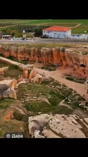 Панорамный вид на остатки древней Дары: красноватые скальные образования, следы раскопок и здание на холме.