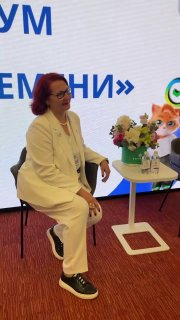 Спикер в белом костюме сидит на стуле на сцене возле стола с цветами во время панели, интерьер конференц-зала и оборудование